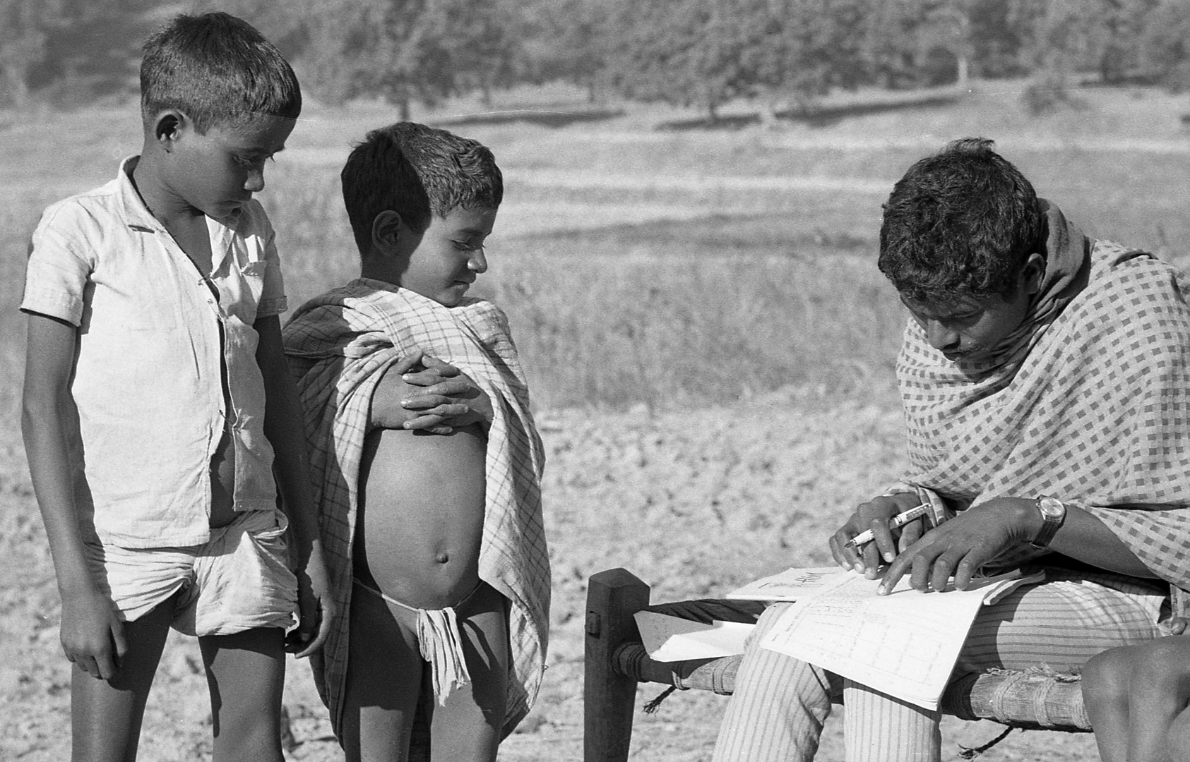 Two boys at the new school in Dubil have their names registered in the daily attendance schedule by the teacher. They look very proud and concerned at this formality, which promises them a literate future.